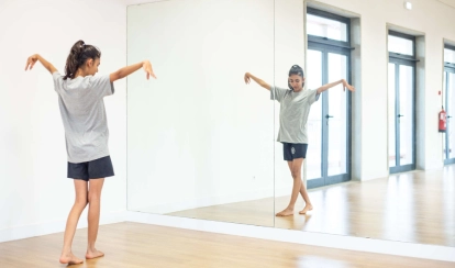 Two students stand together in the library reading a book, surrounded by bookshelves and other students browsing in the background.