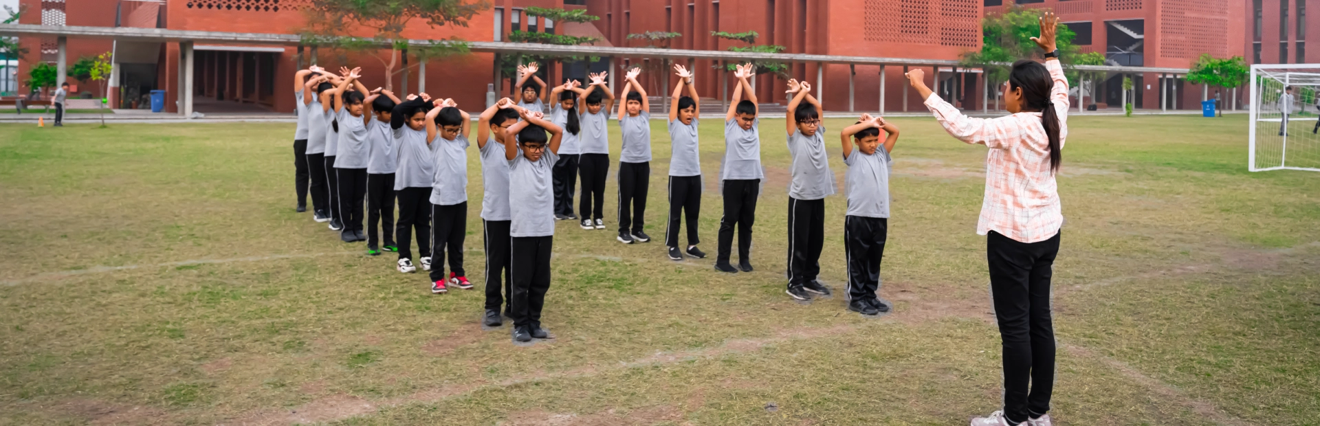 Students perform morning exercises on the school field with a teacher leading the activity at AKA Dhaka.