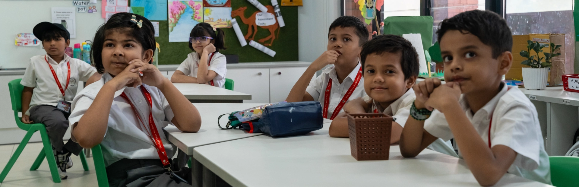 Students sit together in a classroom during a lesson, listening attentively at their desks.