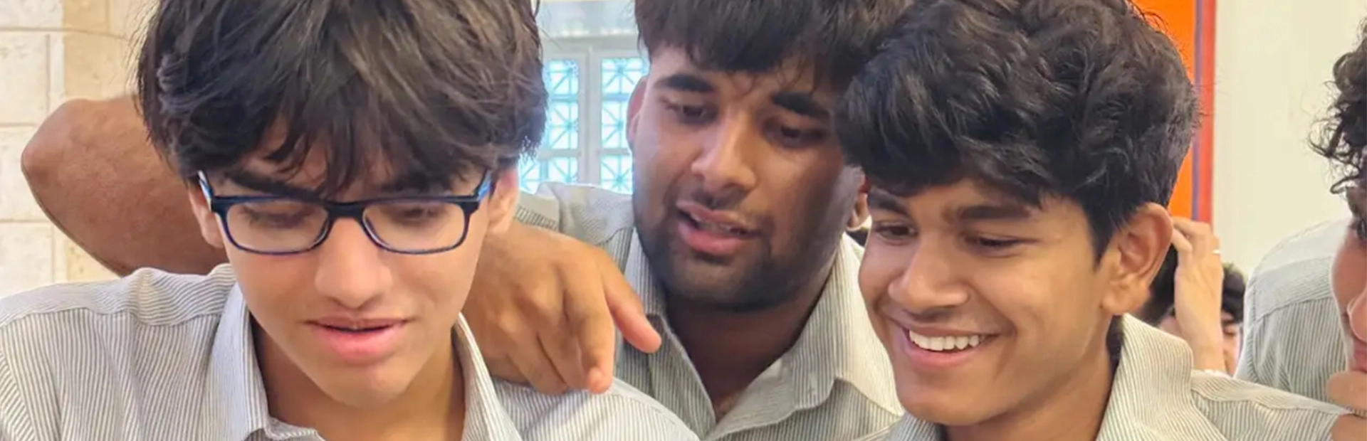  A group of students sitting in chairs with their backs to the camera. A woman is standing at the front of the room in front of a projection on the wall, addressing the students.