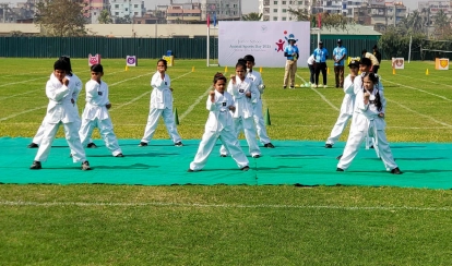 A group of Junior School students dressed in white taekwondo uniforms perform coordinated moves on a green mat during the Annual Sports Day on the school field.