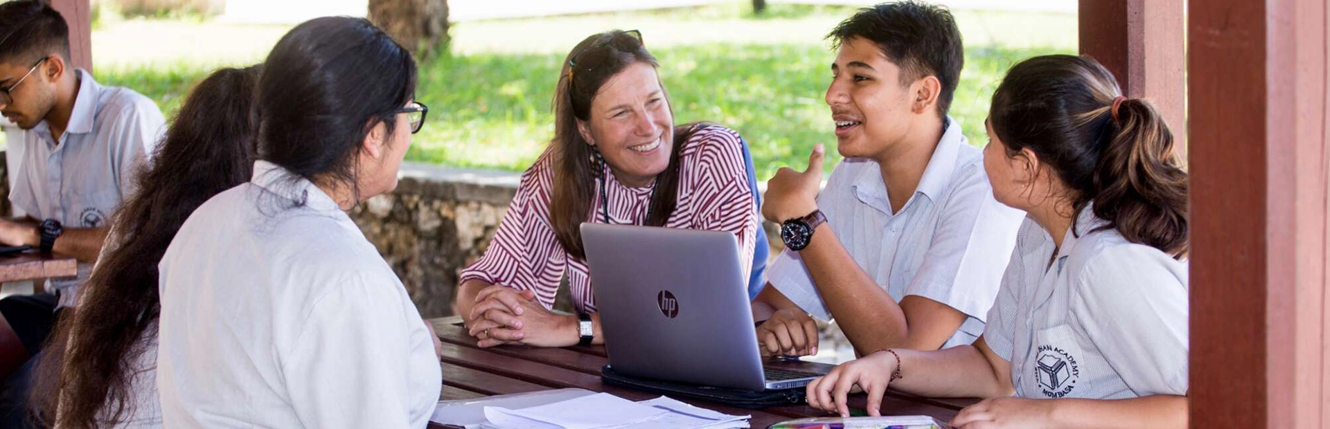 A teacher sits with students outside in a gazebo. 