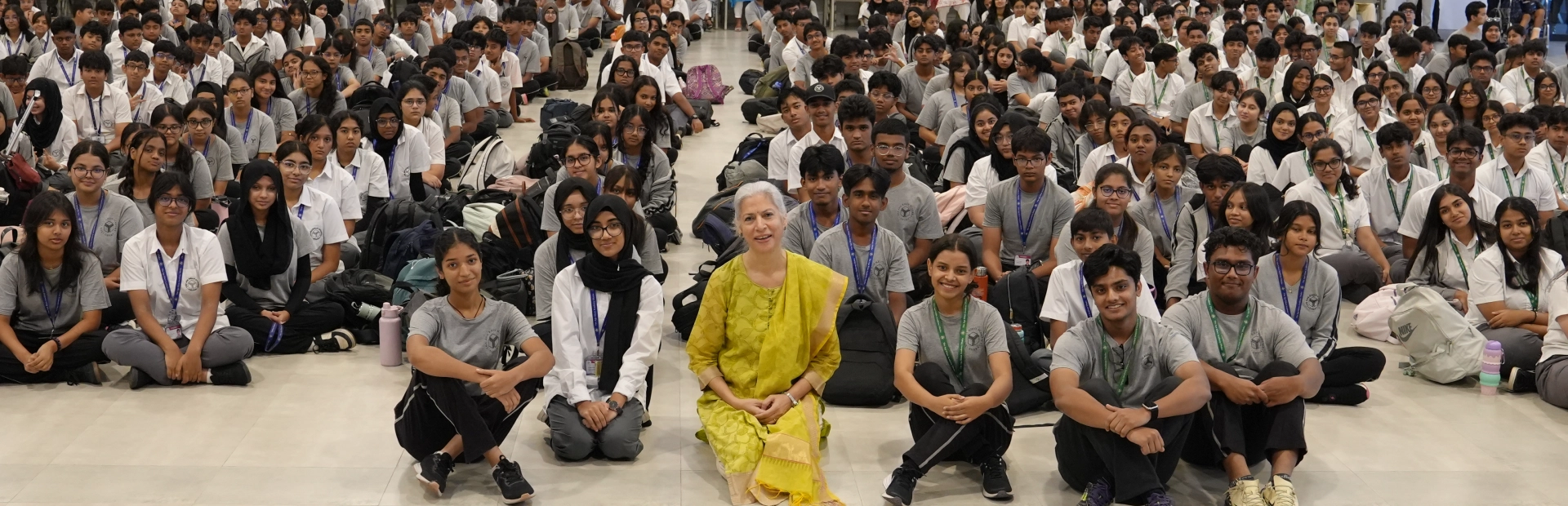 A large group of Senior School students seated on the floor of an assembly hall, facing the camera, with staff members standing behind them.