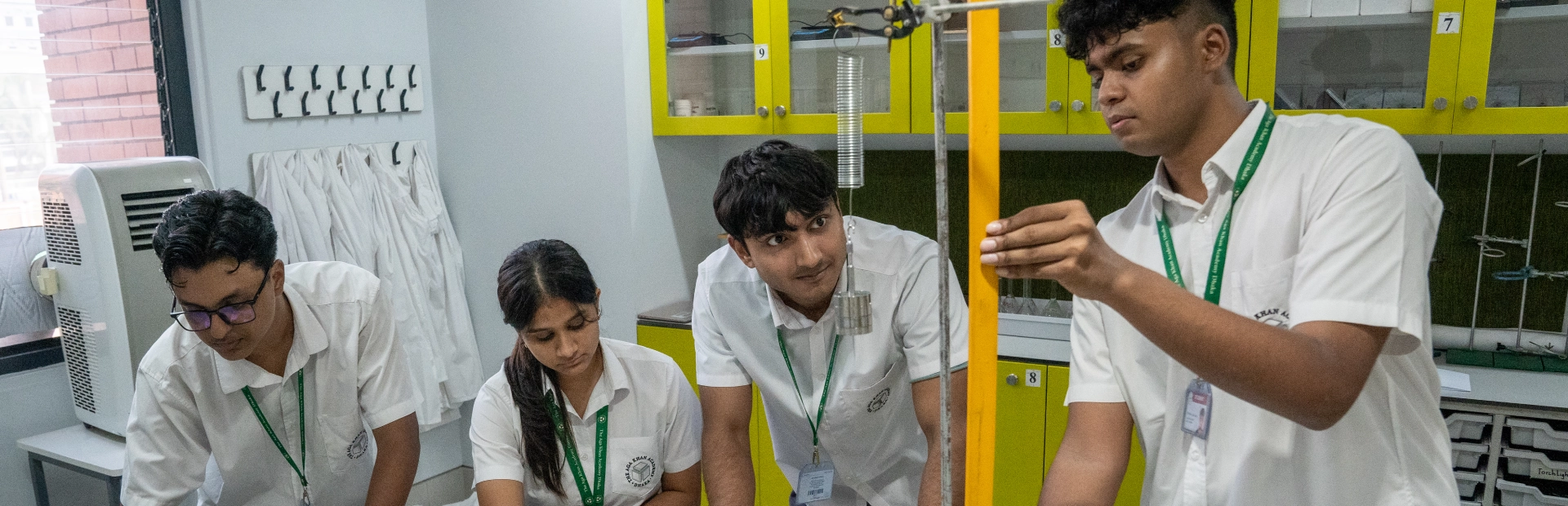 Two students wearing glasses focus on assembling robotic car models at a classroom table. They are handling electronic parts and wires, surrounded by tools and materials.