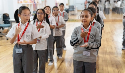 Students in uniform practise rhythmic movements in a classroom.