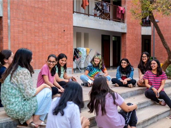 : Aarushi sits in a circle with a group of girls in a circle in front of the girls’ residential block