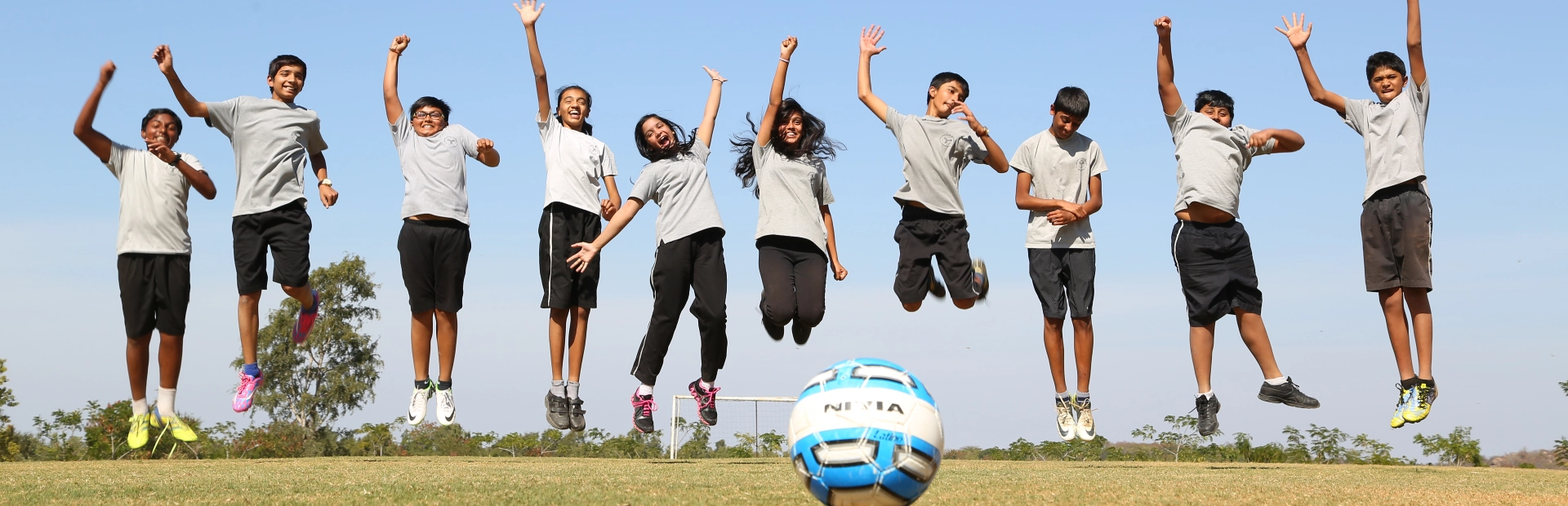 Students jumping in the air on a field, with a football in front of them.
