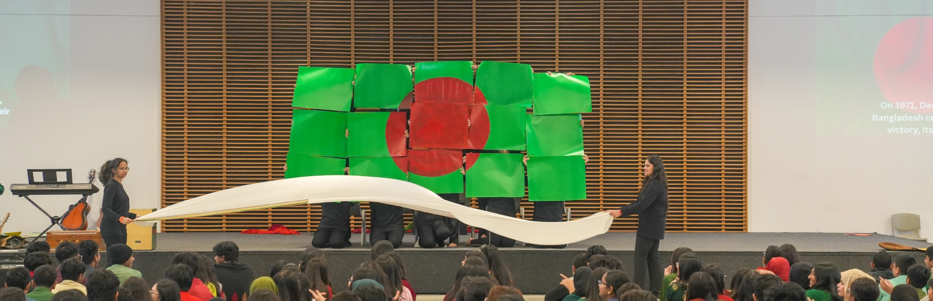 Students hold up the Bangladeshi flag on a stage.