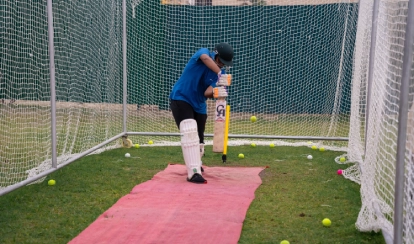 Student bats during cricket practice in a net enclosure.