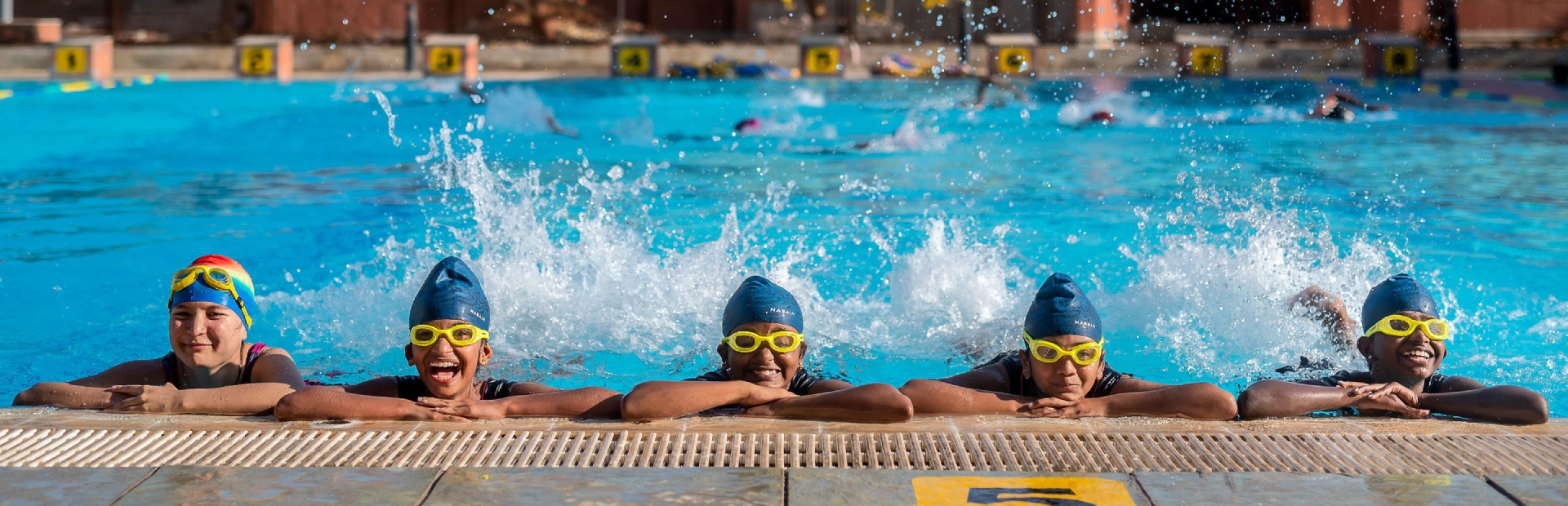 Students gathered at the edge of a pool, looking at the camera and smiling.