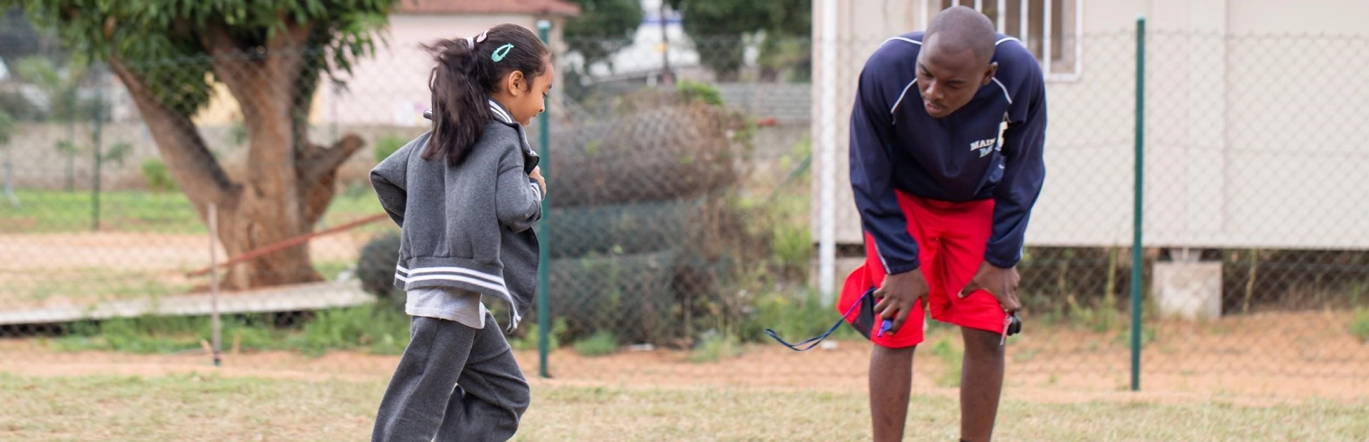  A teacher smiles as she assists two young students shaping clay letters during a classroom activity, with colourful learning materials and displays visible in the background